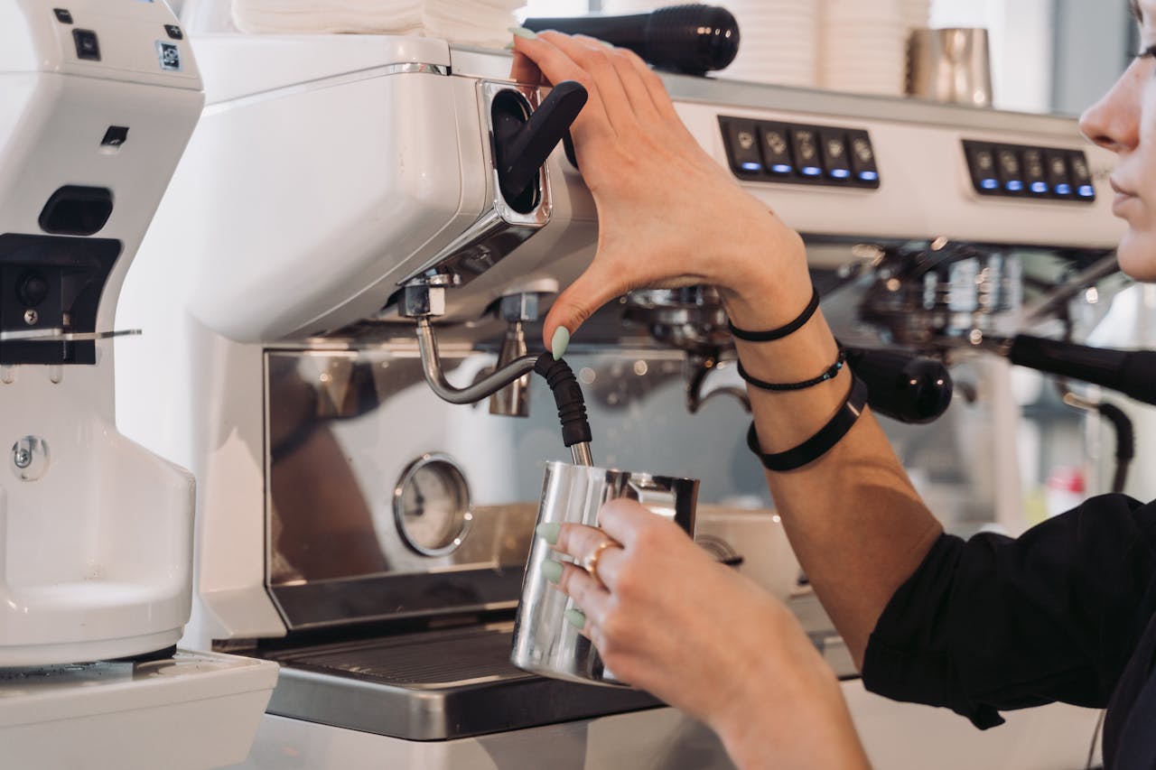 Close-up of barista steaming milk at a modern espresso machine indoors.